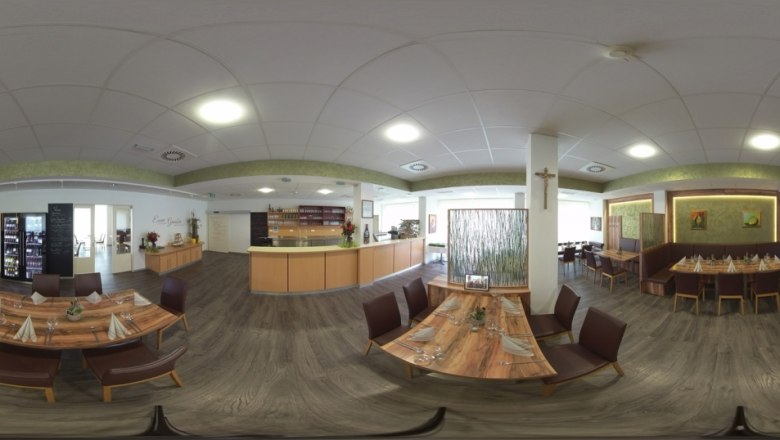 Innenansicht eines modernen Restaurants mit Holztischen und St&uuml;hlen, dekoriert mit Pflanzen und Kunstwerken an den W&auml;nden.