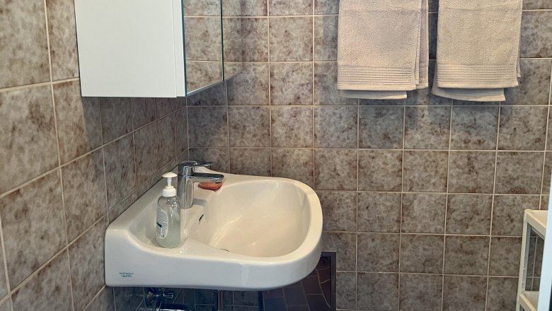 Ein Badezimmer mit Waschbecken, Spiegel, Handt&uuml;chern und Fliesen.