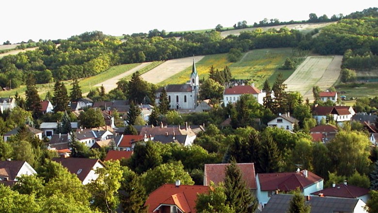 Panorama von Unterolberndorf mit Kirche und umliegenden H&auml;usern vor gr&uuml;nen H&uuml;geln.