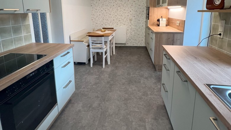 Moderne K&uuml;che mit grauen Schr&auml;nken, Holzakzenten und einem Esstisch. An der Decke eine geometrische Lampe.