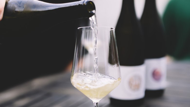 Ein Glas Weißwein wird auf einem Tisch eingeschenkt, mit zwei Weinflaschen im Hintergrund.