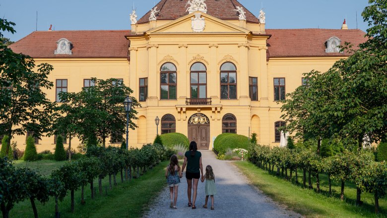 Frau mit zwei M&auml;dchen an der Hand geht auf einem Schotterweg Richtung Schloss Eckartsau.