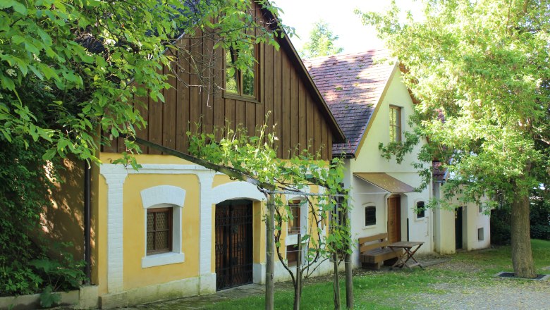 Traditionelle Weinkeller in der Kellergasse von Wolkersdorf, umgeben von grünen Bäumen und Weinreben.