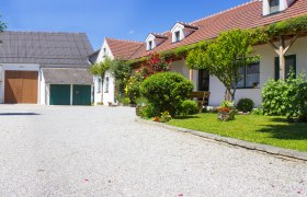 Ein idyllisches Weingut mit Kiesweg, blühenden Gärten und traditionellen Gebäuden unter blauem Himmel.