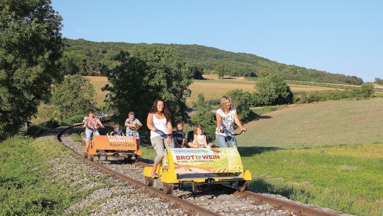 Menschen fahren auf einer Draisine durch eine ländliche Landschaft.