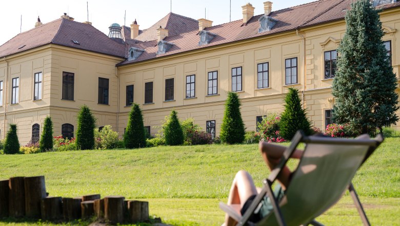 Frau in einem Liegestuhl auf einer gr&uuml;nen Wiese blickt auf Schloss Eckartsau.