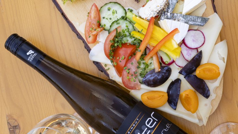 Heurigenplatte mit Aufschnitt, Käse, Gemüse und Wein auf einem Holztisch.