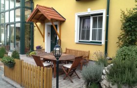 Ein gemütlicher Innenhof mit Holzmöbeln, Pflanzen und gelber Hausfassade.