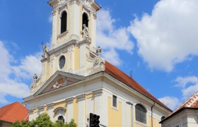 Barocke Kirche mit Turm und Uhr vor blauem Himmel.