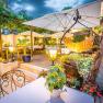 Gastgarten am Abend mit Beleuchtung und vielen Sitzmöglichkeiten, Pflanzen und Schirmen.