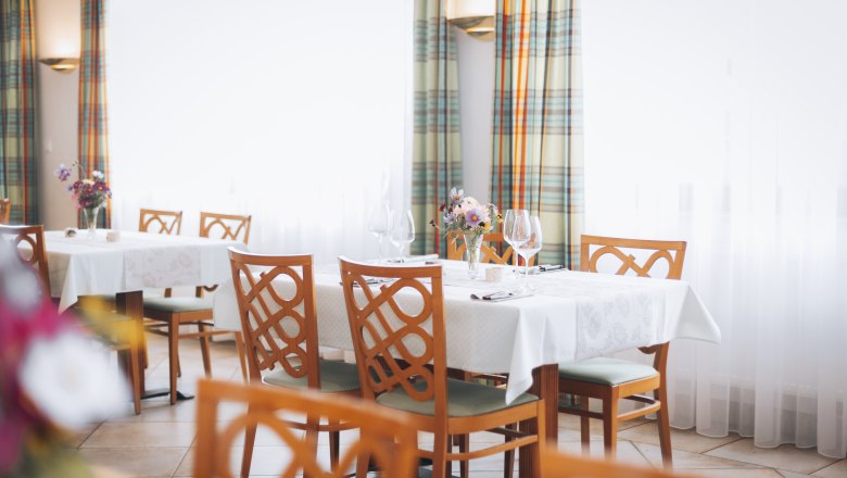 Elegantes Restaurant mit gedeckten Tischen, Blumenarrangements und Weingl&auml;sern.