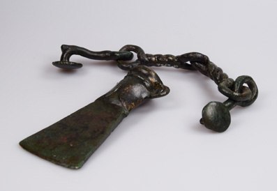 Bronzezeitliches Werkzeug mit Kette auf weißem Hintergrund.