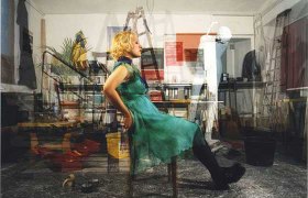 Eine Frau in einem grünen Kleid sitzt in einem überfüllten Raum auf einem Stuhl.