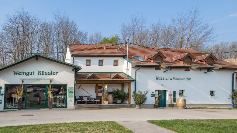 Weingut K&uuml;ssler mit Weinbar und Terrasse, umgeben von B&auml;umen.