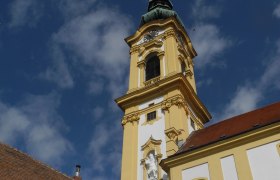 Gelber Kirchturm der Stadtpfarrkirche Stockerau vor blauem Himmel.