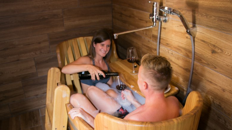 Zwei Personen in einer Holzwannendusche mit Wein.