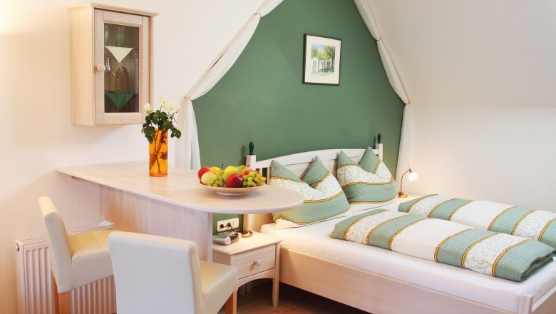 Gem&uuml;tliches Schlafzimmer mit gr&uuml;n-wei&szlig;er Bettw&auml;sche, Holzm&ouml;beln und Dekorationen.