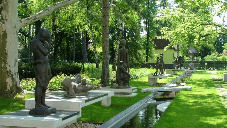 Skulpturen im Park von Bad Pirawarth, umgeben von B&auml;umen und einem kleinen Wasserlauf.