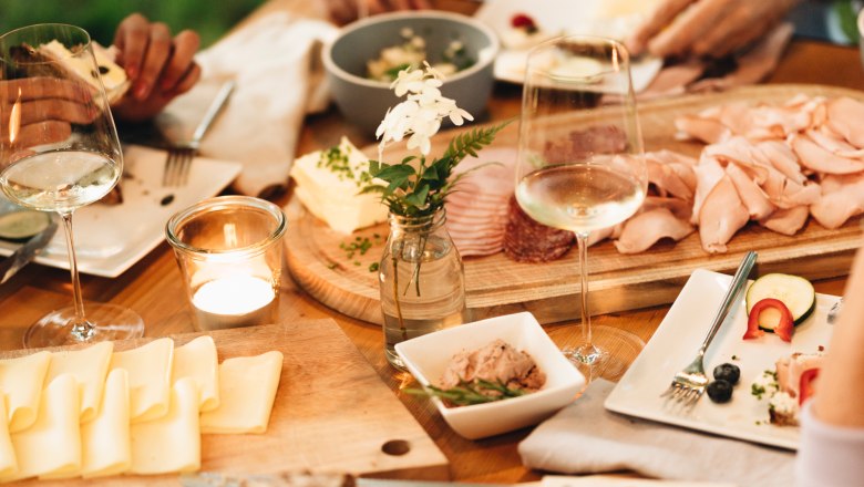 Ein gedeckter Tisch mit Brot, K&auml;se, Aufschnitt und Weingl&auml;sern im Freien.