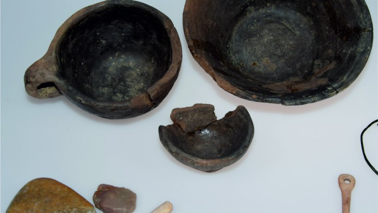 Prähistorische Artefakte wie Schalen, Werkzeuge und Steine auf weißem Hintergrund.