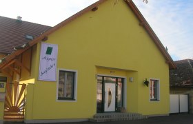 Gelbes Geb&auml;ude mit einem Schild "Aigner Ausg'steckt is" an der Fassade.