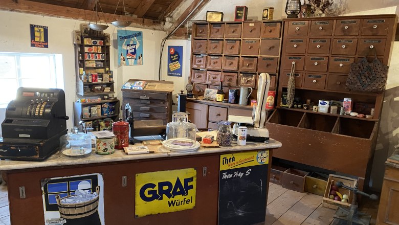 Innenansicht eines historischen Tante-Emma-Ladens mit alter Registrierkasse, Waage und Regalen voller Waren.