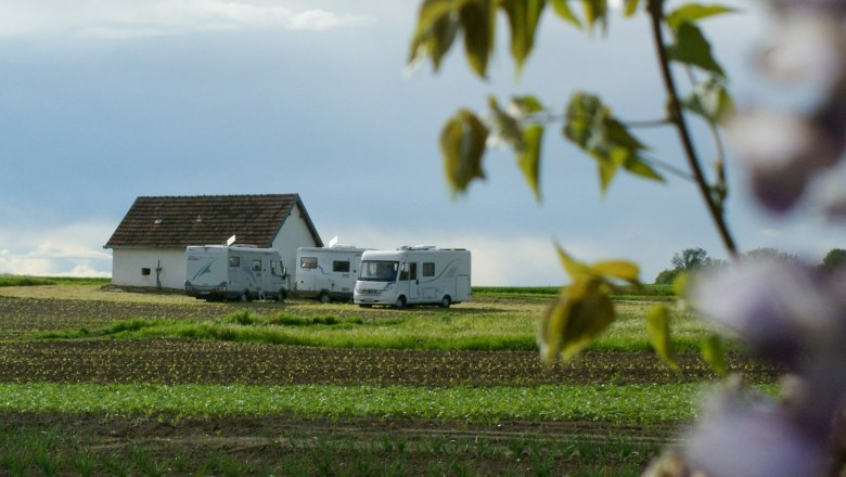 Wohnmobile auf einem Feld neben einem kleinen Geb&auml;ude, umgeben von gr&uuml;ner Landschaft und einem bew&ouml;lkten Himmel.