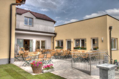 Ein gemütlicher Außenbereich mit Holztischen und -stühlen vor einem gelben Gebäude.